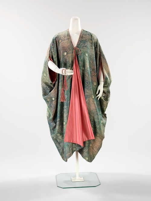 Evening Coat by Liberty & Company, 1910-1915. In the collection of, and image via, the Metropolitan Museum of Art. The London store, Liberty & Company opened its doors in 1875 at a time of heightened Japonism in Europe, and at first was solely dedicated to selling Asian wares.  The company eventually expanded to selling fabrics and fashions of its own design. Both the coat and cape employ Liberty’s “Hera” pattern.  The peacock was an intimate friend of the Greek goddess, who placed the many eyes of her faithful servant Argus on its tail. “Hera” was one of Liberty’s most successful fabrics and is still associated with the company today.  
